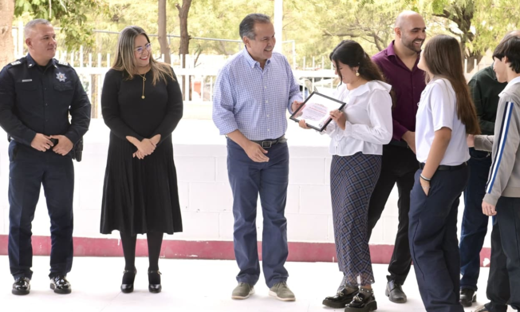 Reconoce Toño Astiazarán a estudiantes de la secundaria 9 que ganaron concurso de calaveras con material reciclado Lunes 9 de Marzo de 2026 En el marco de la ceremonia de Lunes Cívico en la secundaria 9, arquitecto Gustavo F. Aguilar Beltrán, el Presidente Municipal Antonio Astiazarán Gutiérrez destacó el triunfo del plantel en el concurso de calaveras con material reciclado al que convocó la Dirección de Servicios Públicos Municipales y en el que ganaron de entre 25 escuelas. “Siempre he dicho, queridas amigas y amigos, jóvenes aquí de esta gran escuela secundaria número 9, decirles que el Gobierno solo no puede, que para una ciudad es muy importante que todas y todos entendamos que la ciudad no es otra cosa más que la extensión de nuestra propia casa, y por eso estamos obligados a cuidarla como si fuera nuestro propio hogar”, reflexionó ante alumnado, docentes y directivos de la escuela. Toño Astiazarán encabezó la ceremonia de Lunes Cívico y formalizó la incursión de esta secundaria en el programa Reciclase con la entrega de una estación de reciclaje, un contenedor de 1.3 metros cúbicos de capacidad, 20 arbolitos de especies nativas e insumos para el mantenimiento de las instalaciones. Consideró los encuentros con las comunidades escolares como una gran oportunidad de compartir información sobre acciones del Ayuntamiento para el cuidado del medio ambiente, el impacto positivo logrado con las patrullas eléctricas y que conozcan algunas de las unidades y vehículos utilitarios eléctricos que distinguen a Hermosillo. “Sigamos haciendo ejemplo y que se oiga muy fuerte en toda la H que la secundaria número 9 es la campeona en el reciclaje de nuestra ciudad”, externó luego de entregar a la maestra Ana Isabel Ulloa Álvarez y a sus alumnas y alumnos, su reconocimiento como ganadores del concurso de calaveras hechas con materiales de desecho reciclables. Astiazarán Gutiérrez estuvo acompañado por Jesús Alonso Durón Montaño, Comisario General de la Policía Preventiva y Tránsito Municipal; Sergio Arturo Pavlovich Escalante, director de Servicios Públicos Municipales y David Galván, coordinador de zona del programa CRECES. Los recibieron Jorge Luis González Fimbres y Cora Patricia Mora, director y directora de la escuela respectivamente y Fausto Blanco Dávalos supervisor de zona escolar y como invitadas acudieron las regidoras Dulce Robles y Carla Salcido. Previo a la ceremonia cívica, las botargas UMPI de Bomberos de Hermosillo; Tina Gotina, de Agua de Hermosillo y Reciclara, de Servicios Públicos Municipales, saludaron a las alumnas y alumnos y amenizaron la ocasión con bailes y expresiones de camaradería.